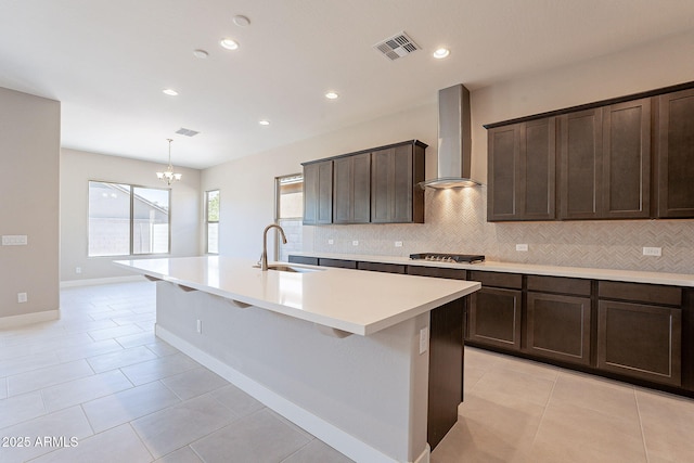 kitchen with an island with sink, wall chimney exhaust hood, sink, and light tile patterned floors