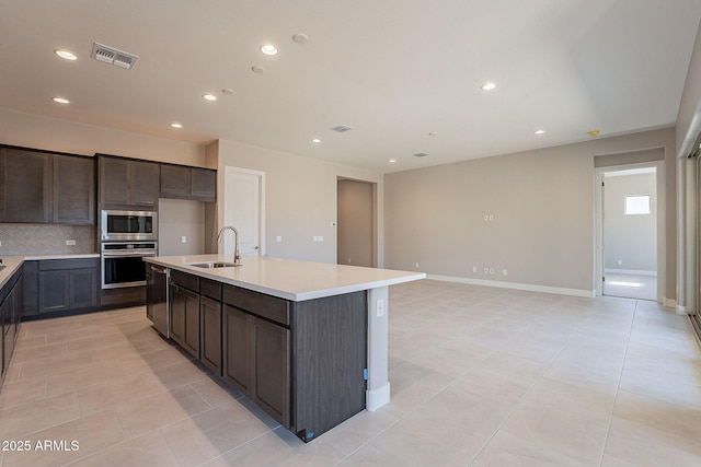 kitchen featuring light tile patterned flooring, sink, tasteful backsplash, stainless steel appliances, and a kitchen island with sink