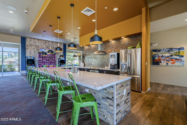 kitchen with stainless steel fridge, a spacious island, decorative light fixtures, light stone counters, and a breakfast bar area