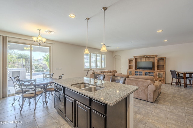 kitchen with pendant lighting, dishwasher, sink, a kitchen island with sink, and light stone counters