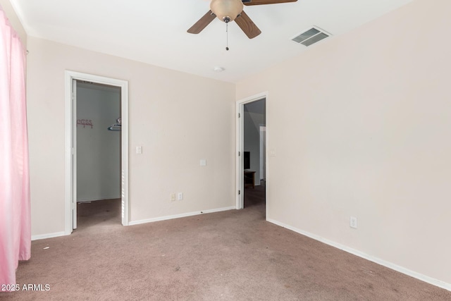 unfurnished bedroom featuring a walk in closet, light carpet, ceiling fan, and a closet