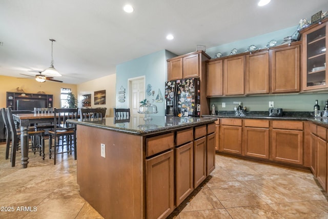 kitchen featuring black fridge, a center island, hanging light fixtures, dark stone countertops, and ceiling fan