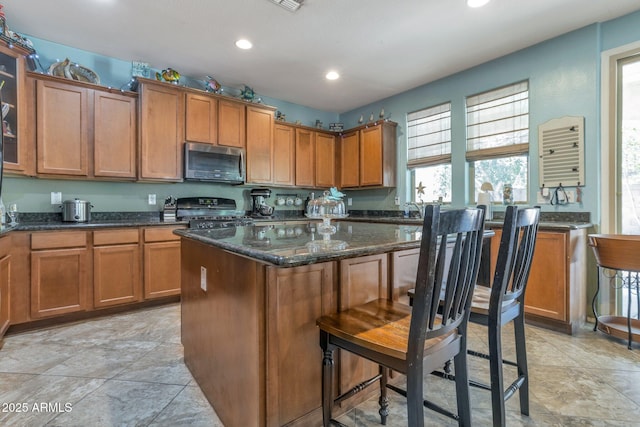 kitchen with a breakfast bar, sink, black range oven, a center island, and dark stone counters