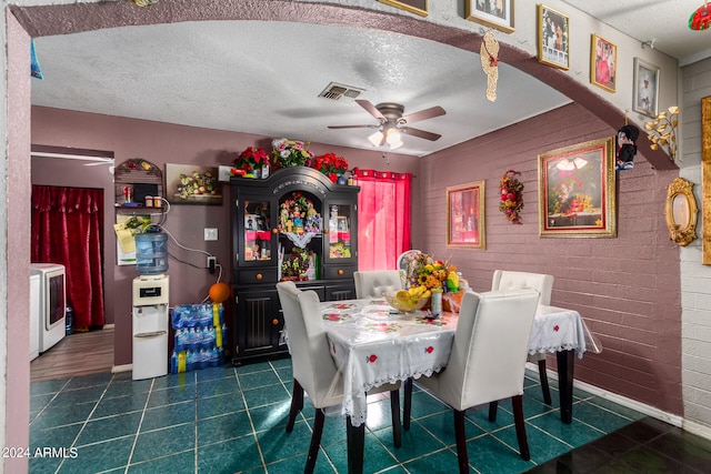 tiled dining area featuring ceiling fan, brick wall, washer / clothes dryer, and a textured ceiling