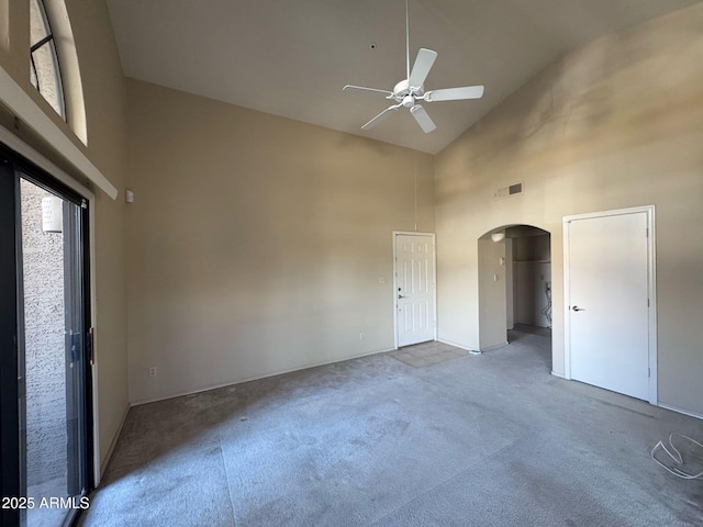 carpeted empty room featuring high vaulted ceiling, arched walkways, visible vents, and a ceiling fan