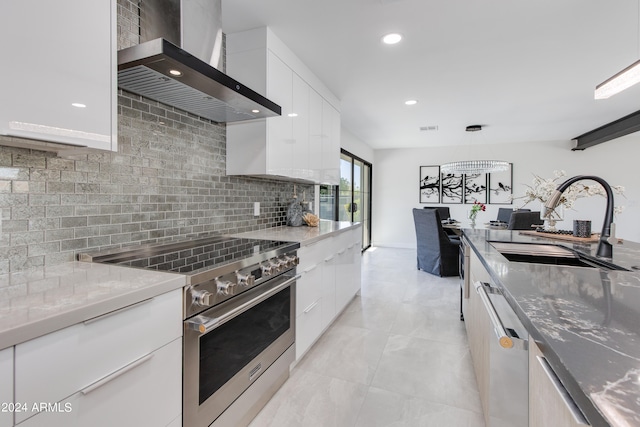 kitchen with wall chimney range hood, sink, white cabinets, and stainless steel appliances