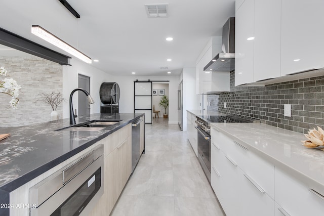 kitchen featuring light tile flooring, hanging light fixtures, wall chimney exhaust hood, sink, and appliances with stainless steel finishes