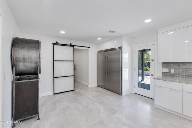 kitchen with built in fridge, a barn door, white cabinetry, and light tile floors