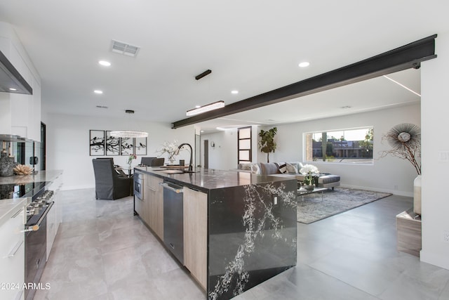 kitchen featuring dark stone counters, an island with sink, beam ceiling, appliances with stainless steel finishes, and light tile floors