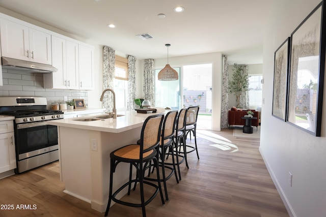 kitchen featuring visible vents, stainless steel range with gas stovetop, backsplash, under cabinet range hood, and a sink