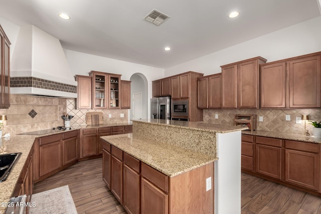 kitchen featuring custom exhaust hood, light stone counters, appliances with stainless steel finishes, dark hardwood / wood-style floors, and a kitchen island