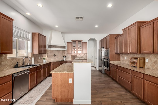 kitchen with sink, custom exhaust hood, a center island, stainless steel appliances, and light stone countertops