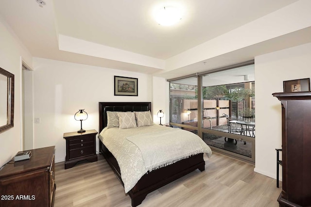 bedroom with light wood-style floors, access to outside, and a raised ceiling