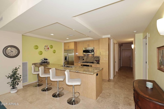 kitchen with stainless steel appliances, a peninsula, a sink, visible vents, and tasteful backsplash