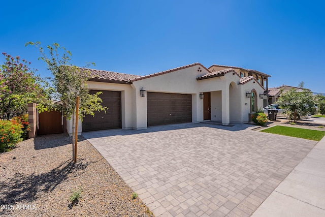 mediterranean / spanish-style home featuring a garage, decorative driveway, stucco siding, and a tile roof