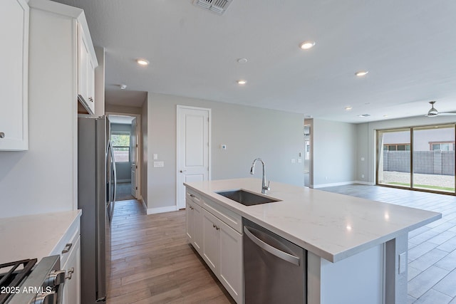 kitchen with a sink, stainless steel appliances, light wood finished floors, white cabinets, and recessed lighting