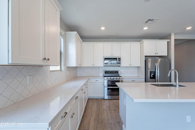 kitchen featuring stainless steel appliances, a sink, white cabinets, light stone countertops, and recessed lighting