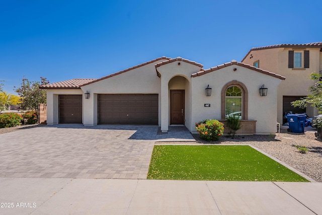 mediterranean / spanish-style home featuring stucco siding, an attached garage, a tile roof, and decorative driveway