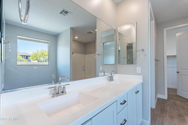 bathroom with a shower stall, wood finished floors, baseboards, and double vanity