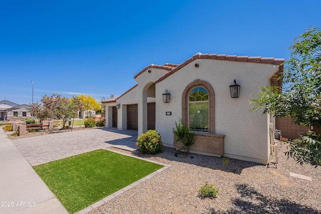 mediterranean / spanish home with an attached garage, decorative driveway, stucco siding, and a tiled roof