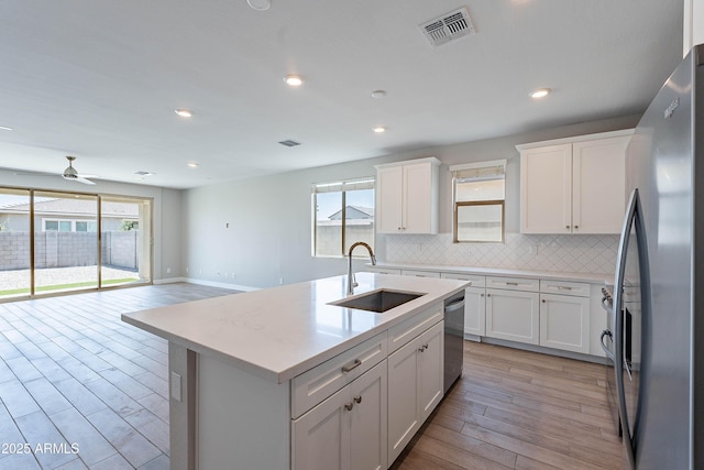 kitchen featuring stainless steel appliances, a sink, light wood finished floors, decorative backsplash, and white cabinetry