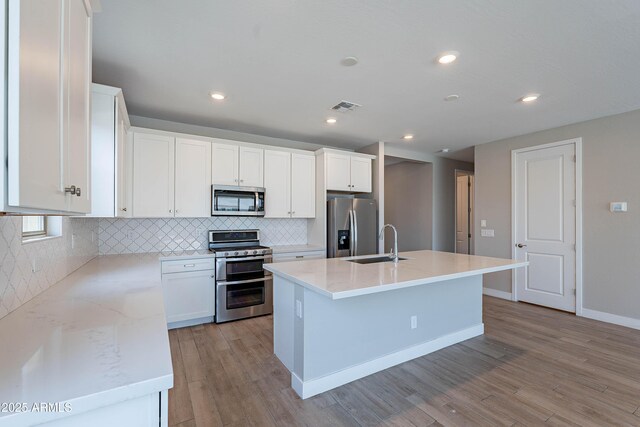 kitchen with appliances with stainless steel finishes, a sink, light wood-style flooring, decorative backsplash, and white cabinetry