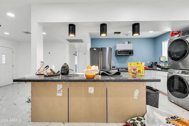 kitchen with white cabinetry, stacked washer / drying machine, stainless steel appliances, and a kitchen bar