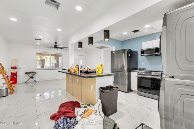 kitchen with stacked washer / dryer, dark stone countertops, a kitchen island, ceiling fan, and appliances with stainless steel finishes