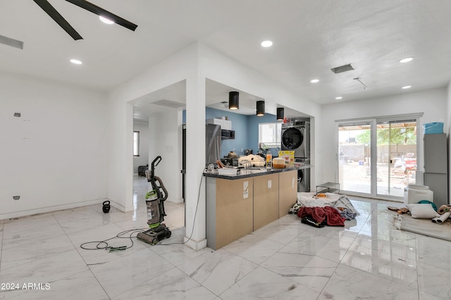 kitchen featuring ceiling fan, dark stone counters, stacked washing maching and dryer, and light tile patterned floors