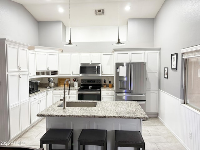 kitchen with light stone countertops, a kitchen island with sink, appliances with stainless steel finishes, and pendant lighting