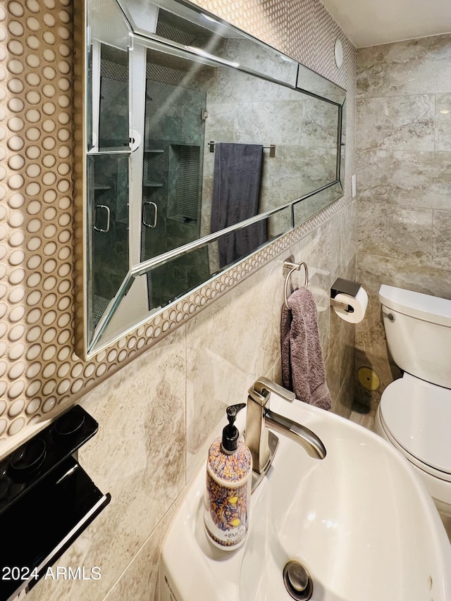 bathroom with a shower with door, a sink, tile walls, and toilet