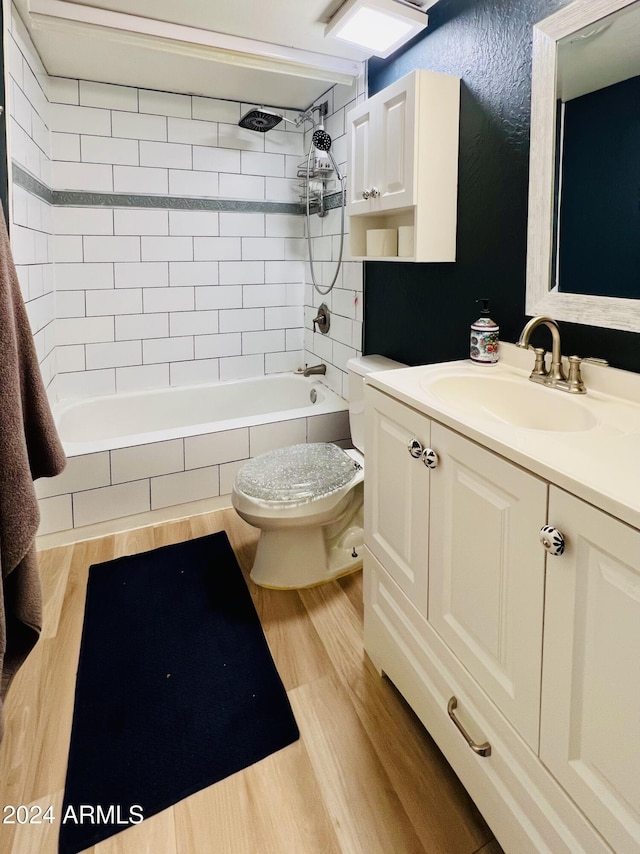 full bath featuring toilet, tiled shower / bath, wood finished floors, and vanity