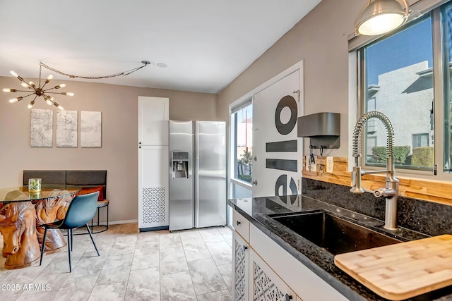 kitchen with a chandelier, white cabinets, stainless steel fridge, and a sink