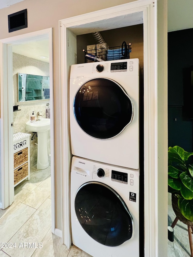 laundry room featuring sink, light tile patterned floors, and stacked washer and dryer