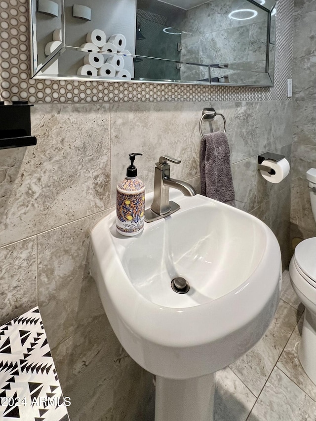 bathroom featuring toilet, marble finish floor, tile walls, and a sink