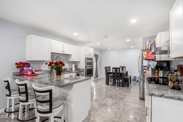 kitchen featuring stone countertops, white cabinets, a breakfast bar, a peninsula, and stainless steel double oven