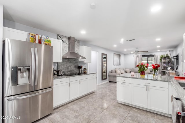 kitchen with light stone counters, white cabinetry, open floor plan, appliances with stainless steel finishes, and wall chimney range hood