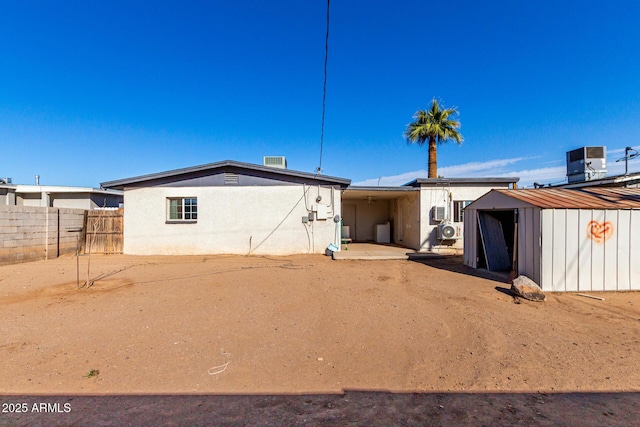 rear view of property featuring an outbuilding, central air condition unit, stucco siding, fence, and a shed