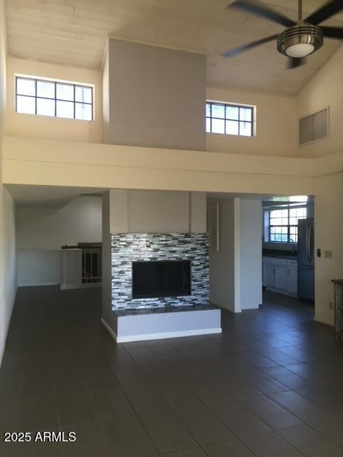 unfurnished living room with a tile fireplace, ceiling fan, and a high ceiling