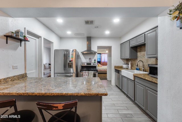 kitchen with sink, appliances with stainless steel finishes, a kitchen breakfast bar, kitchen peninsula, and wall chimney range hood