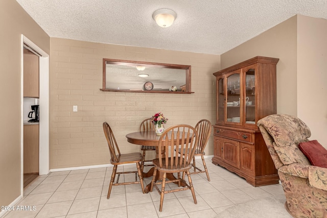 dining area featuring light tile patterned floors, brick wall, and a textured ceiling