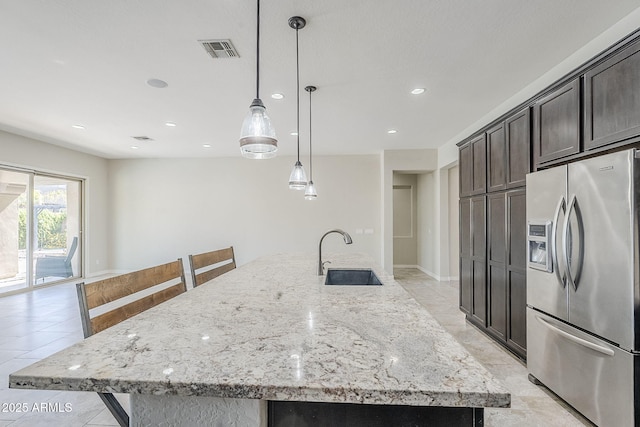 kitchen with stainless steel fridge with ice dispenser, a sink, recessed lighting, a large island with sink, and light stone counters