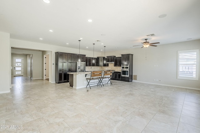kitchen with appliances with stainless steel finishes, open floor plan, a kitchen bar, a kitchen island, and ceiling fan
