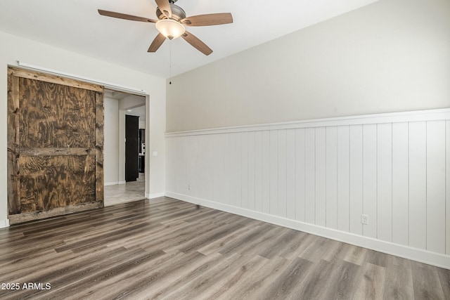 spare room featuring wood finished floors, a ceiling fan, wainscoting, and baseboards