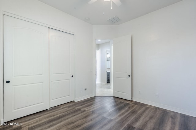 unfurnished bedroom with dark wood finished floors, a closet, baseboards, and ceiling fan
