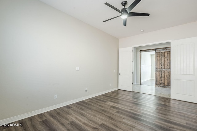 unfurnished bedroom featuring wood finished floors, baseboards, a barn door, and ceiling fan