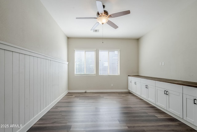spare room with a ceiling fan, dark wood-type flooring, and a wainscoted wall
