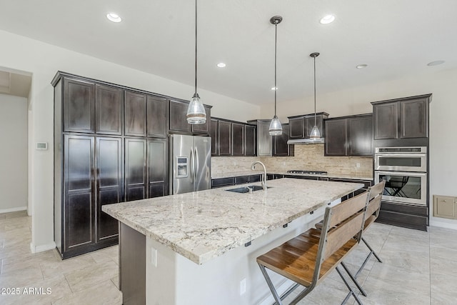 kitchen with appliances with stainless steel finishes, a sink, decorative backsplash, light stone countertops, and baseboards