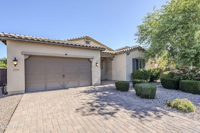 mediterranean / spanish home featuring stucco siding, decorative driveway, an attached garage, and a tile roof