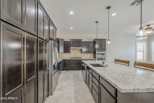kitchen featuring a sink, backsplash, a large island with sink, appliances with stainless steel finishes, and light stone countertops